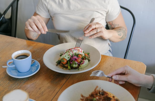 A person using a knife and fork to eat their meal with poached eggs.