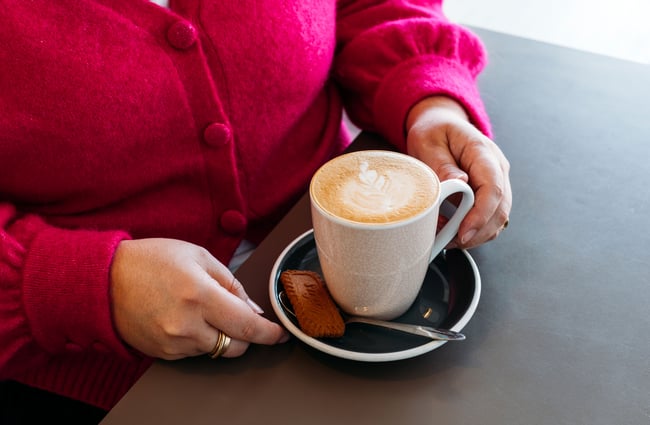 A woman wearing a bright pink cardigan holding a coffee.