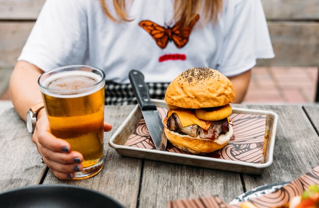 A woman sitting behind a burger and pint of beer.