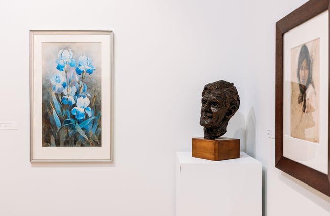 Paintings and a bust on display inside an art gallery.