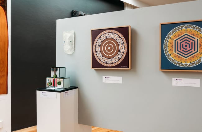 A close up of works of art on display on a white wall.