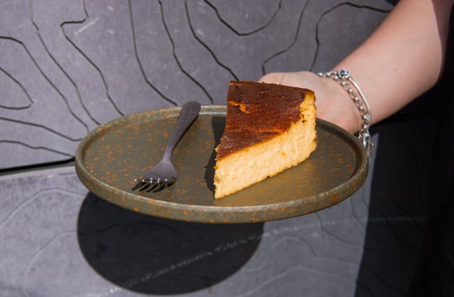 A hand holding a slice of cheese cake on a plate.