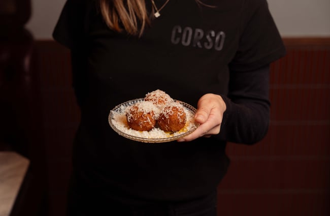 A hand holding a plate of arancini balls.