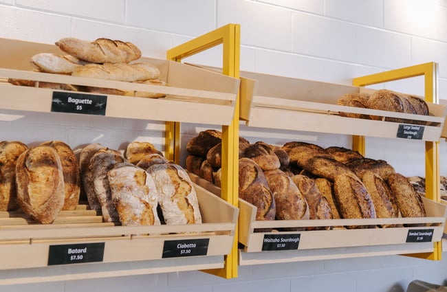 Close up of rows of sourdough on wooden shelves attached to a wall at Bellbird Bakery in Christchurch.