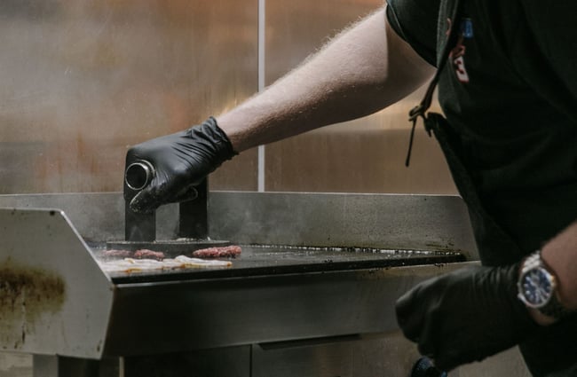 Chef wearing all black cooking over the steaming hot grill.