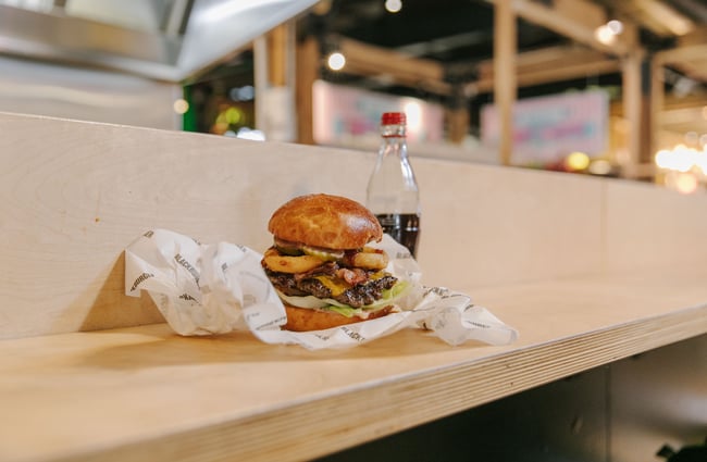 Big burger sitting on the bench unwrapped next to a coke.