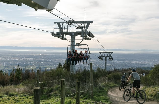 Zip liners coming up the chairlift and bikers riding down a trail at Christchurch Adventure Park.