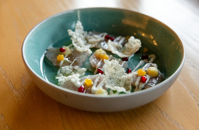 Plate of raw fish topped with red pomegranate jewels, bits of orange fruit and wafer pieces