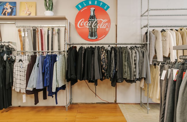 Lots of grey and black jackets on display underneath a Coca a Cola sign.