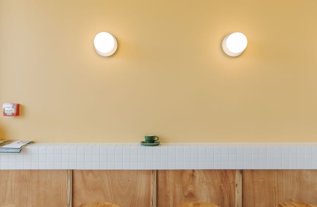 A green coffee cup sitting against a yellow wall.