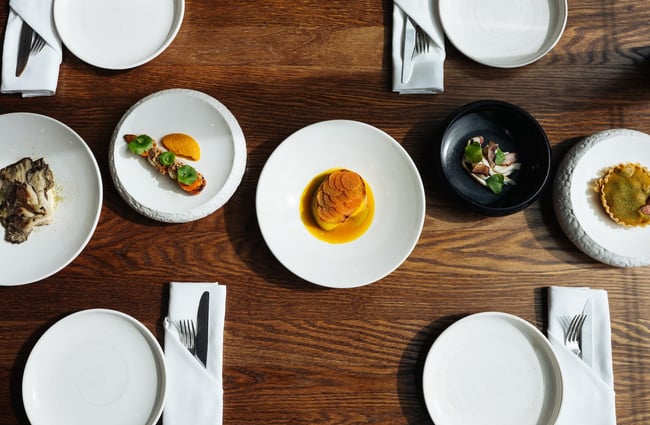 Birds eye view of five dishes down the middle of a table set with white plates and linen napkins.