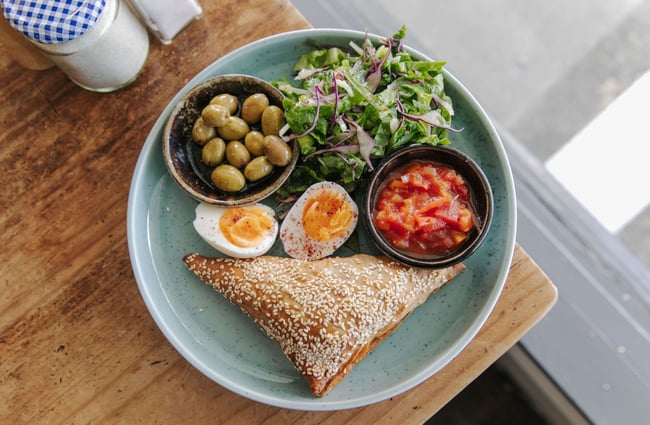 Birds eye view image of the blue plate with salad, eggs, olives and a savoury pastry.