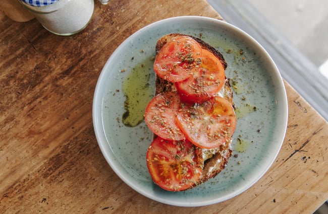 A slice of toast with 5 tomato slices displayed on a blue plate.