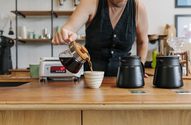 A woman pouring black coffee into a cup.