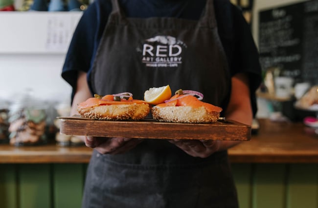 Woman holding a bagel on chopping board.