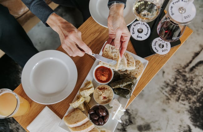 A hand spreading hummus onto a piece of bread above a cheese platter.