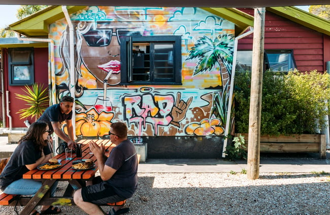 Customers sitting at a picnic table outside Roots Bar on a sunny day.