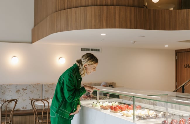 A woman all in green smiling and pointing to a cabinet.