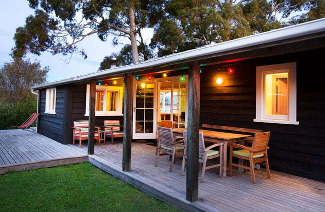 A black painted Apple Pickers' Cottage lit up at dusk.