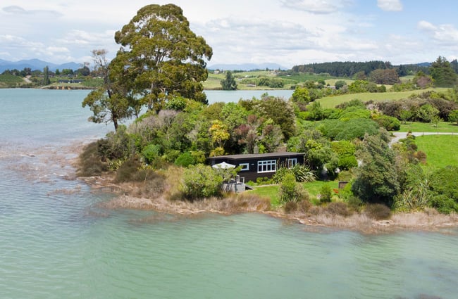 One of the black cottages nestled into trees next to water.