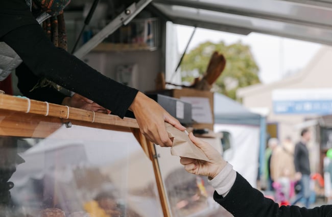 Stallholder passing a customer a brown paper bag at The Nelson Market, Nelson.