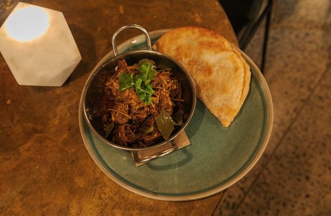 A close up of a bowl of meat with a side of roti.