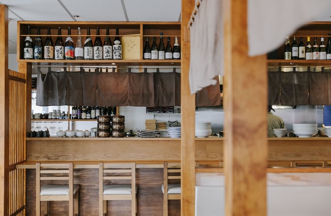 Looking over the counter into the kitchen where the chef is.