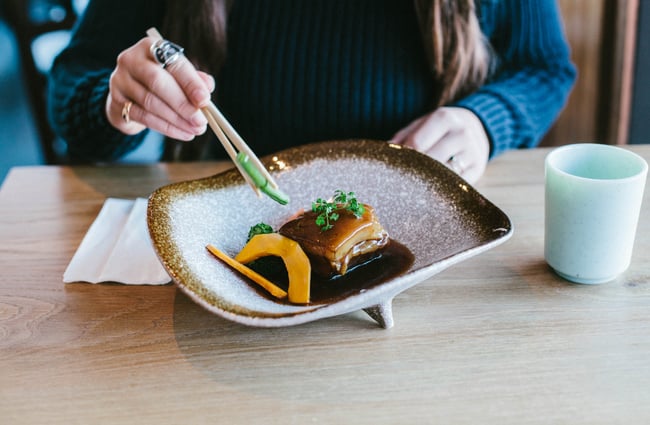 A lady using chopsticks to eat her food at Tomi's.