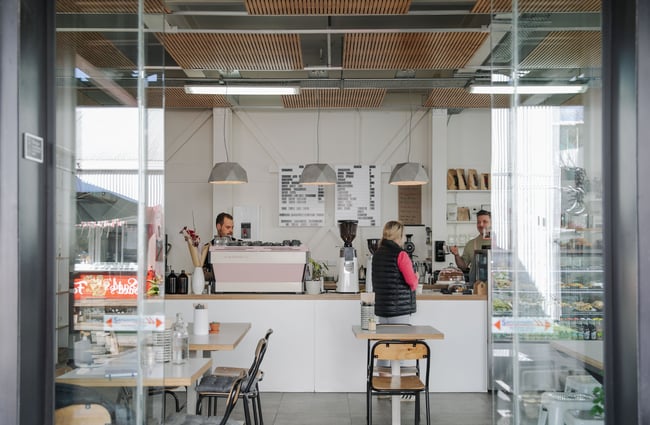 People ordering at the counter where there is a pink and white coffee machine.