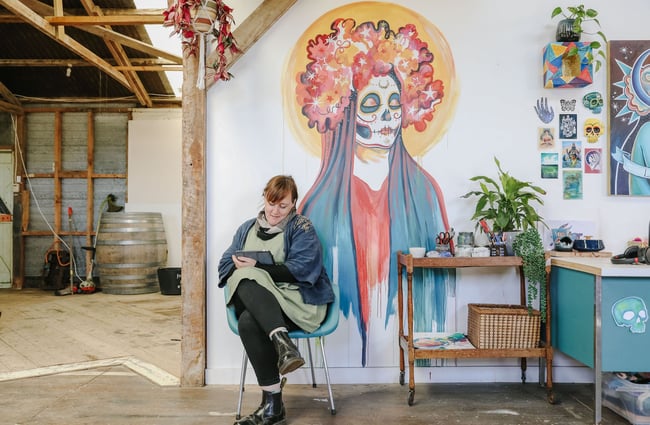 Woman sat by art mural on the wall at Zappekin Artists & Allies, Nelson Tasman.