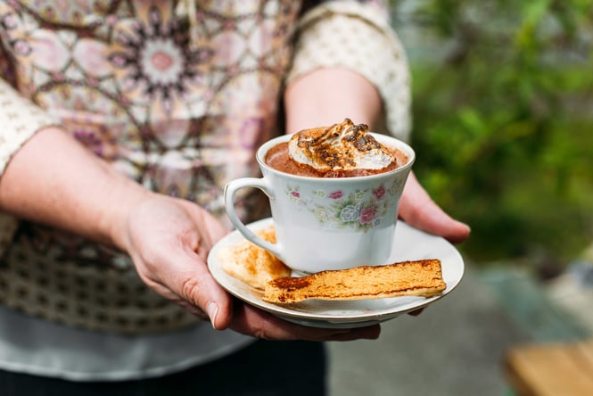 A person holding a china cup and saucer with a smore's hot chocolate.