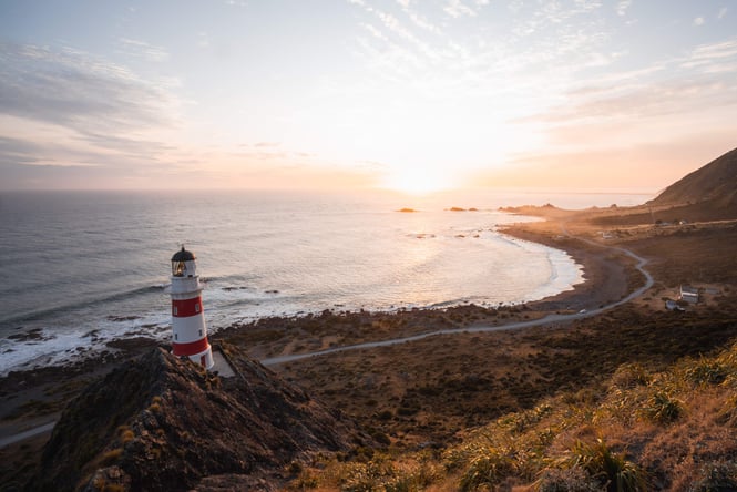 A red and white light house at dusk at Cape Palliser, New Zealand.