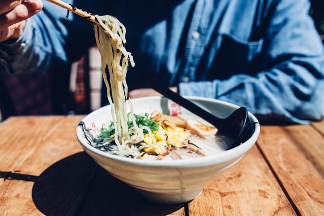 Noodles dangling from chopsticks over a bowl of ramen.