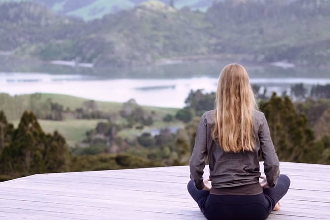 Woman sat on wooden deck doing yoga at Mana Retreat Centre.