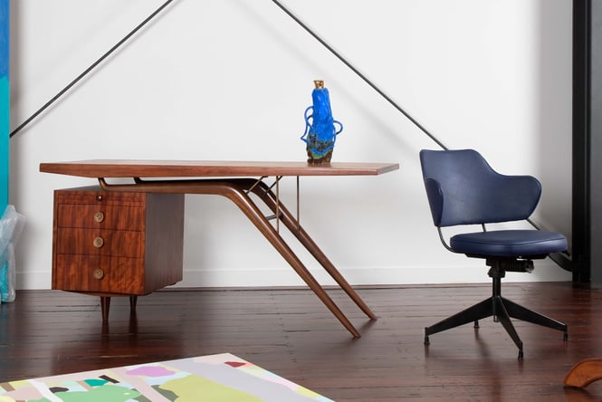 Abstract wooden desk with a dark blue office chair and a blue vase on the desk.