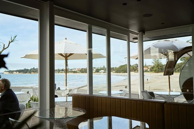 Interior of white contemporary cafe with windows looking out onto Takapuna Beach