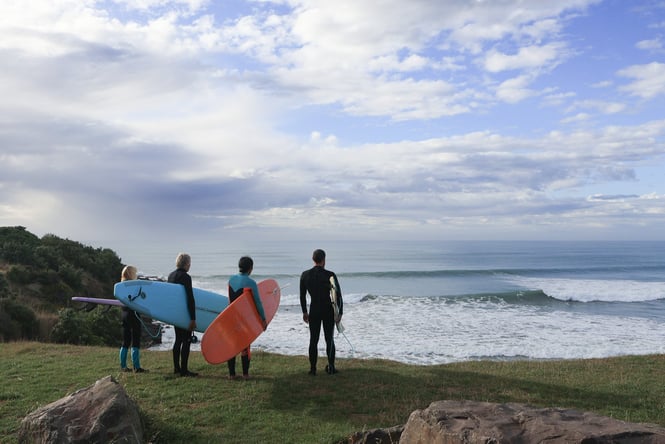 Surfers standing around staring at the ocean.