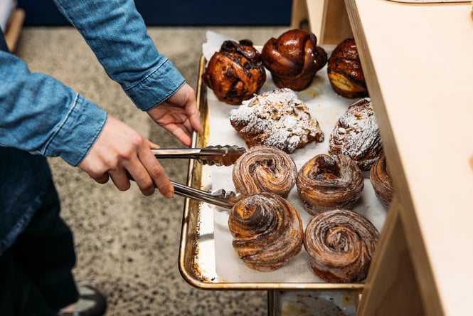 A baker using tongs to pick up a freshly baked morning bun at Rüdi's Bakehouse