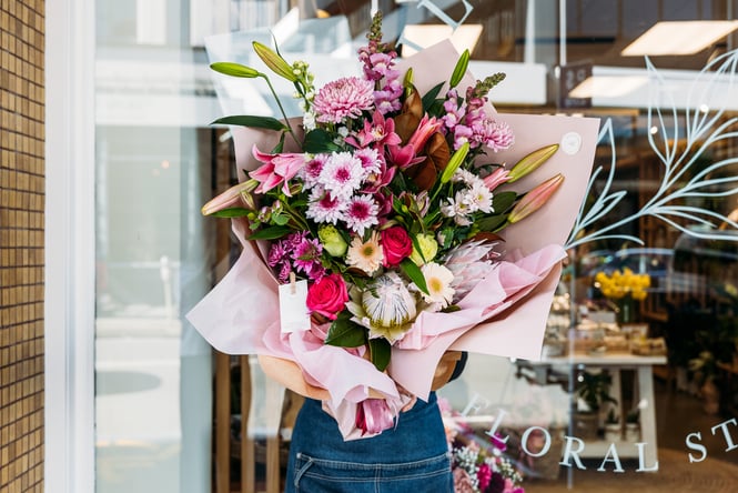 A florist holding up a large bouquet of flowers in front of store