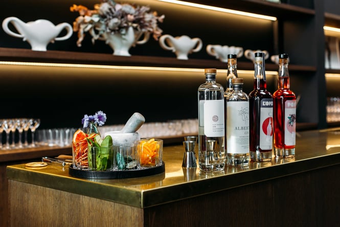 A line up of gin and liquor next to a bowl of fruit and herb garnishes