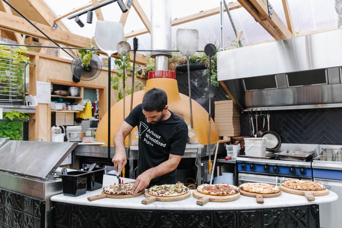 A chef making multiple pizzas at once next to a wood fired oven.