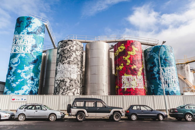 Very tall silos painted in graffiti art on a cloudy day.