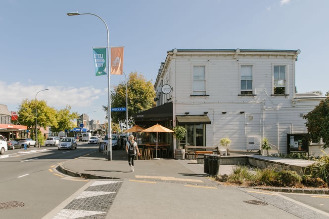 A woman crossing the street in Ponsonby on a sunny day.