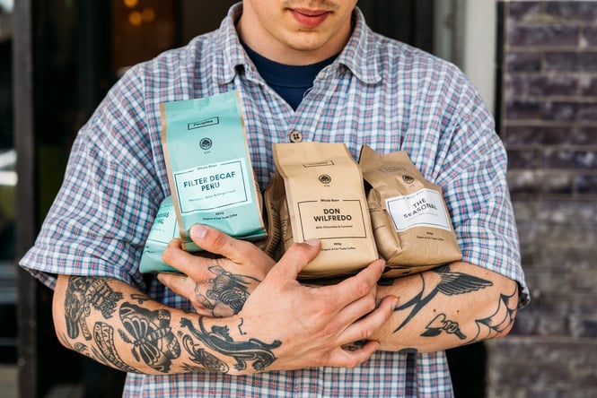 A tattooed man holding bags of freshly roasted coffee