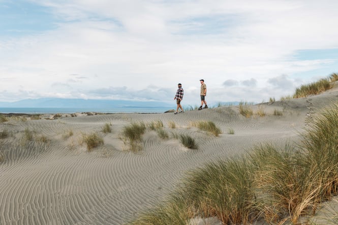 Two men walking along the beach on a sunny day.