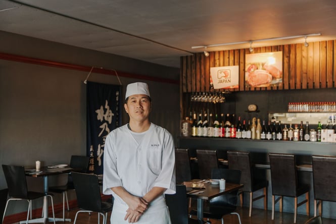 The Chef of Kinji Japanese restaurant standing in the middle of the restaurant smiling.