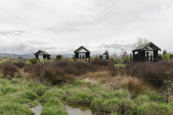 Looking across green and brown tussocks where there are 4 huts.