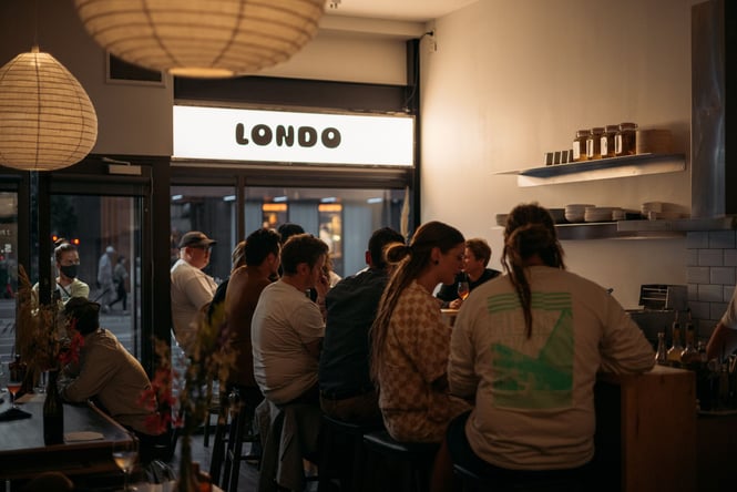 People sitting at the bar seating with a big group of people.