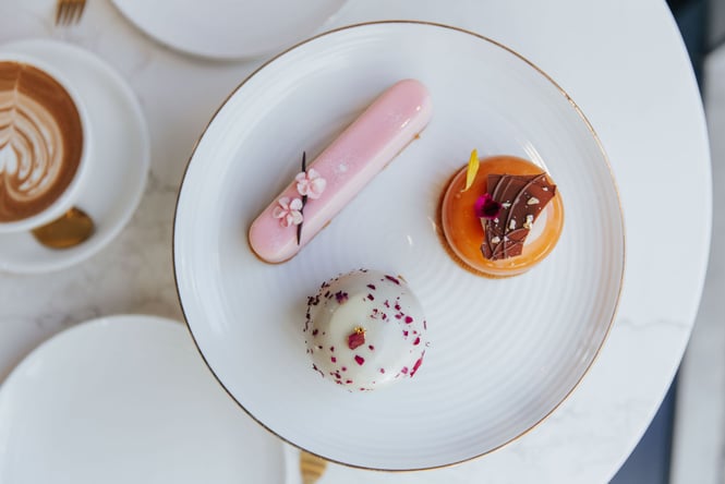 A pink, orange and white pastries on a white plate with a flat white coffee.