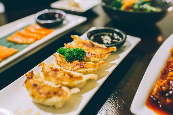 Dumplings and sliced salmon on plates on a black table.